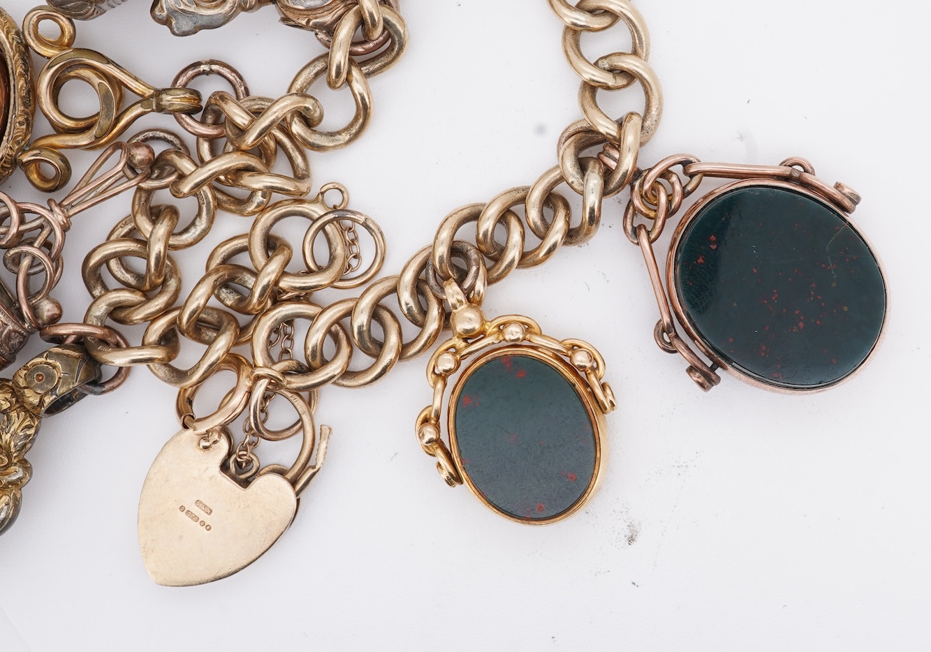 A 1970's 9ct gold curb link charm bracelet, with 9ct gold heart shaped clasp, hung with seven assorted gold or gilt metal mounted charms including six chalcedony set fob seals, gross weight 73 grams.